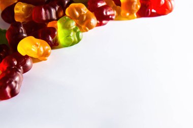 Çerçevenin sol üst köşesinde farklı renklerde meyve suyu bulunan jelibon hayvanları beyaz arka planda yatar.