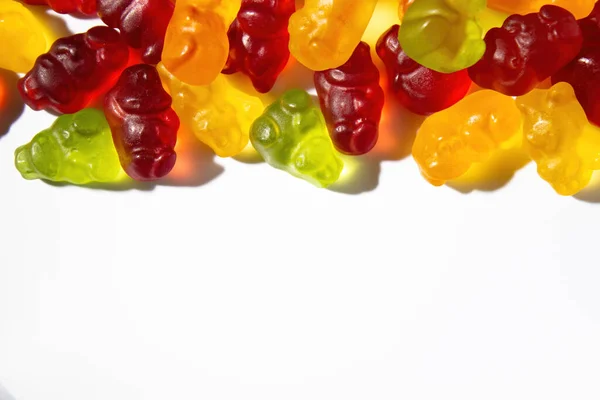 Gummy animals of different colors with fruit juice lie on top of the frame on a white background