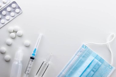 Soldaki beyaz arka planda yuvarlak beyaz haplar var, iki kabarcık hap, damlalar, bir şırınga, bir ampul ilaç. doğru tıbbi maske