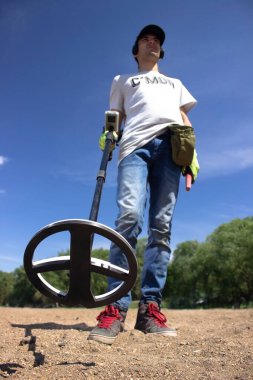 Kablosuz kulaklıklı bir adam kumsalda elinde kablosuz metal dedektörü tutuyor.