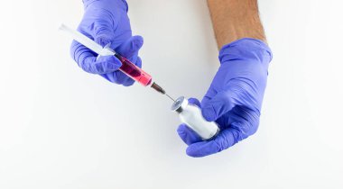 a disposable syringe with a needle and an ampoule with red (vitamin B12) liquid in male hands in blue (lilac) nitrile gloves.  On a white background, lots of empty space