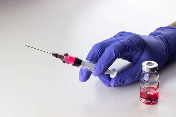 a disposable syringe with a needle and an ampoule with red (vitamin B12) liquid in male hands in blue (lilac) nitrile gloves.  On a white background, lots of empty space