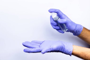 A man's hand in a blue medical glove sprays an antiseptic from a vial onto a second gloved hand.  On a white background.  Lots of empty space