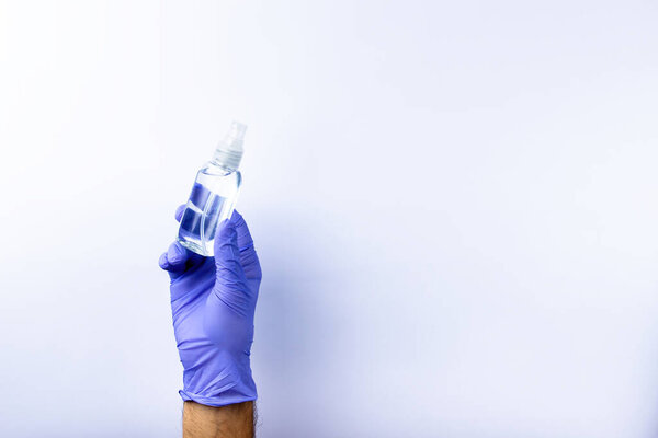 A human hand in a blue medical glove holds a plastic bottle with an antiseptic, on a white background.  Lots of empty space