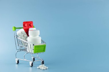 On a blue background in a shopping cart are various medical supplies, medicines.  Lots of free space