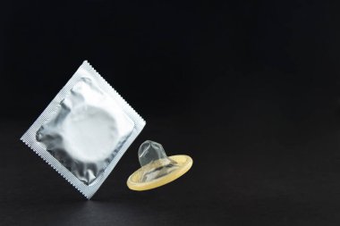 An unpacked condom and one in a foil package levitate on a black background.  Lots of empty space. Safe sex and reproductive health concept. 