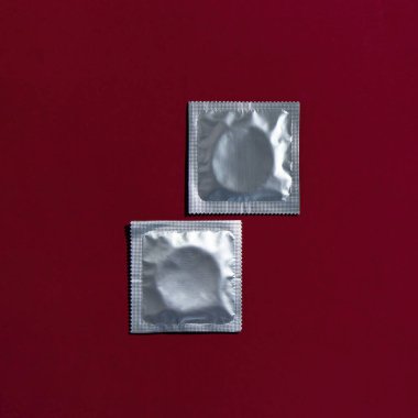 Two condoms in foil packaging lie on a dark red background. Safe sex and reproductive health concept.