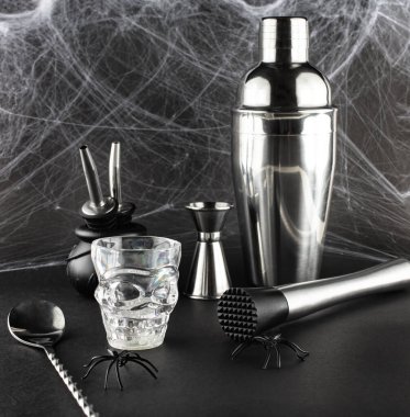 Çeşitli bar aksesuarları: bir titretici, karıştırıcı, süzgeç, bir bar kaşığı ve bir ölçü yığını gibi siyah bir matte masasında bir örümcek ağının zemininde yatar. Yetişkinler bayramı kutlaması