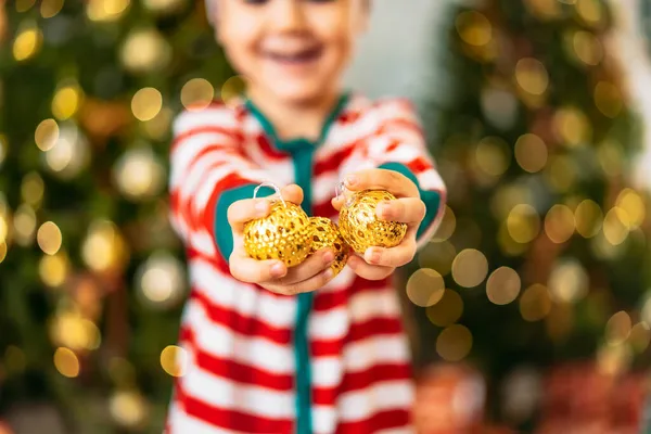 Noel ağacının arka planında Noel oyuncakları olan küçük bir çocuğun elleri. Tatil konsepti.