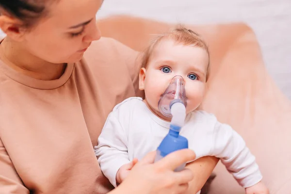 Evde küçük bir kız astım spreyinden nebulizör soluyor. Solunum maskesi takmış viral hastalığı olan bir çocuk annesinin kollarında oturuyor. Astımı olan hasta.