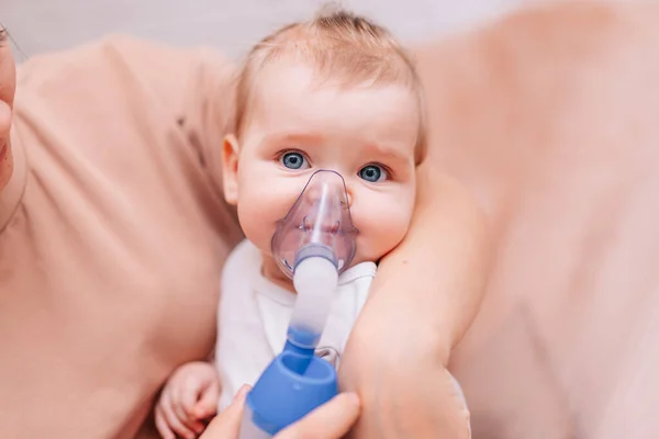 Evde küçük bir kız astım spreyinden nebulizör soluyor. Solunum maskesi takmış viral hastalığı olan bir çocuk annesinin kollarında oturuyor. Astımı olan hasta.
