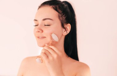 Jade Gouache ile yüz gerdirme ameliyatı için masaj. Avrupalı görünümlü, yüzü için silindir kullanan güzel esmer bir kadın. Evde cilt bakımının güzelliği.