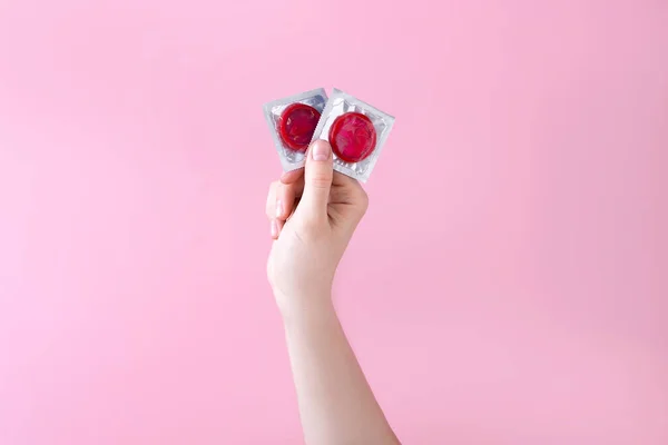 Deux préservatifs de couleur rouge dans une main de femme, sur un beau fond rose. concept de protection — Photo