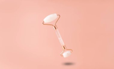 Rose Quartz Gua sha 'dan yapılmış yüz silindiri. Bej bir arka planda havada asılı duruyor. düz yat