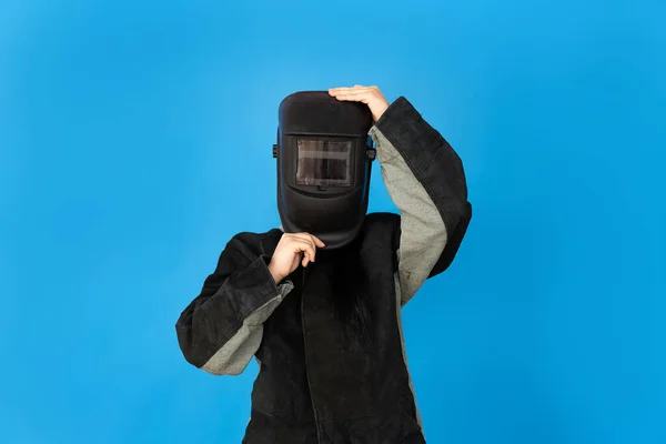 Üniformalı bir kadın kaynakçı, koruyucu kask takıyor, mavi arka planda izole edilmiş.