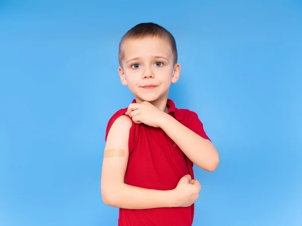 在蓝色背景下接种疫苗后 快乐的男孩肩膀上有一块贴片 这是针对考拉韦病毒或Covid 19疫苗的概念 — 图库照片