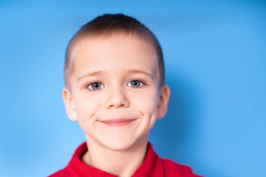 Mavi arka planda, kameraya bakan sevimli, mutlu bir çocuğun fotoğrafı.