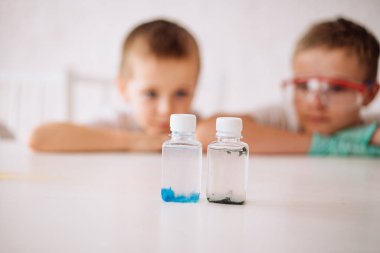 Küçük çocuklar deneyler yapıyor, çocuklar kimyasal çözeltisi olan şişeleri izliyor. Çocukların erken gelişimi. Araştırma ve geliştirme kavramı.