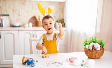 Avrupalı görünümlü yakışıklı bir çocuk masaya güler ve kafasına sarı tavşan kulakları çizer.
