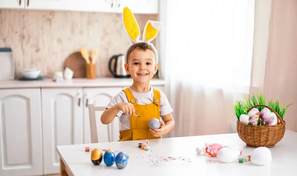 Avrupalı görünümlü yakışıklı bir çocuk masaya güler ve kafasına sarı tavşan kulakları çizer.