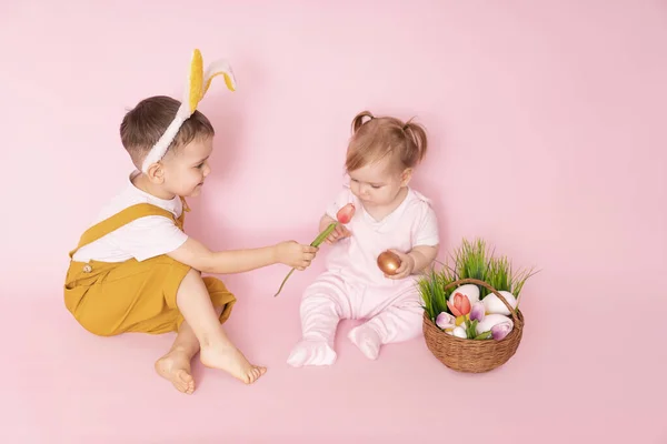 复活节快乐的孩子们在兔子耳朵里 孩子们带着复活节兔子和鸡蛋 是的一个粉红背景的男孩和一个女孩 — 图库照片