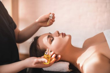 Genç ve güzel bir kadın kaplıcada masaj yaptırıyor. Masör yüzüne masaj yağı damlatıyor. Spa bakımı konsepti