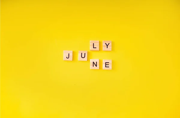 Das Wort lautet Juni Juli, geschrieben in Holzbuchstaben. Juni-Text auf gelbem Hintergrund für Ihr Design, Draufsicht-Konzept. Platz für Text — Stockfoto