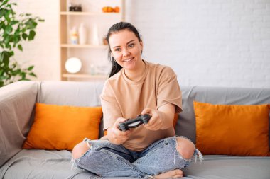 Çekici esmer kadın evdeki kanepede video oyunları oynuyor.