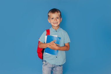 Elinde defterleri olan küçük neşeli bir çocuk. Mavi bir arka planda izole edilmiş..