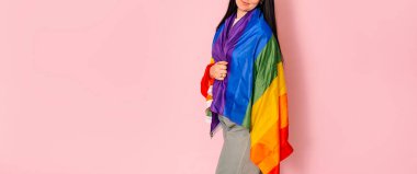 LGBT konsepti. Siyah saçlı pozitif bir kız gökkuşağı bayrağı tutuyor, pembe arka planda bir stüdyoda izole edilmiş..