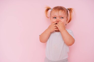 Pembe arka planda izole edilmiş ağlayan iki yaşında bir kızın yakın çekimi.