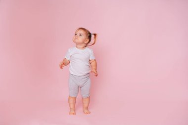 Sevimli küçük mutlu kız pembe bir arka planda duruyor, çocuk eşyalarının reklamını yapıyor..