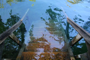 Ahşap merdiven mavi şeffaf suya giriyor.