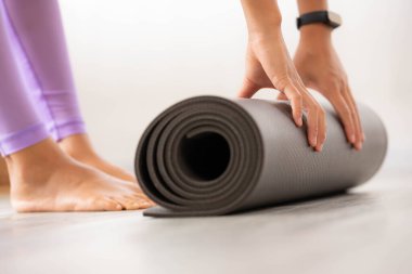 Asyalı kadın egzersiz minderini kaldırıyor ve yoga yapmaya hazırlanıyor. Sabahın erken saatlerinde evde paspasın üstünde egzersiz yapıyor..