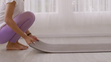 Asyalı bir kadının elleri bir egzersiz minderini kaldırıyor ve yoga yapmaya hazırlanıyor. Sabahın erken saatlerinde evde paspasın üstünde egzersiz yapıyor..