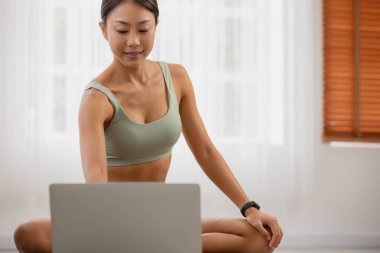 Asyalı kadın evde dinleniyor. Sabah yogaya başlayıp bilgisayarı açıp sınıfa katılıyorsun..