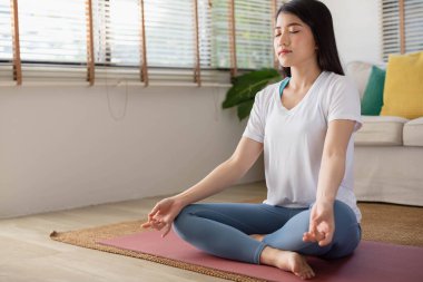 Asyalı bir kadınla sabah yogası, kolay bir pozisyonda oturmak, Sukhasana duruşu ve internette meditasyon yapmak..
