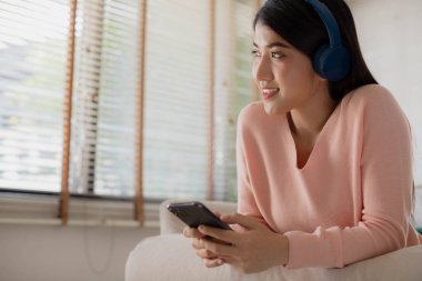 Asyalı kadın akıllı telefonunu kullanıyor. Müzik dinlemek için kulaklık kullanır. Bir şarkıyı dinlemek ya da meditasyon sesi dinlemek size huzur, iç uyum ve denge hissi verir..