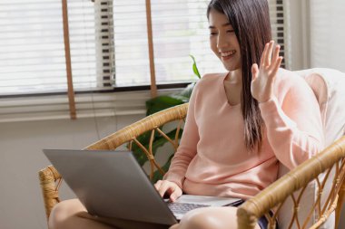 İş yerinde video konferansı var. Ofisinde, Asyalı bir kadın bilgisayar kullanarak görüntülü görüşme yapıyor. Çeşitli etnik gruplardan oluşan bir şirket ekibi. Kendi evinin rahatlığından.