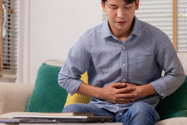 Karnında ağrı, ishal, hazımsızlık sorunu olan Asyalı bir adamın eli. Evde mide ağrısı çeken mutsuz bir adam.