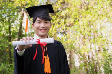 Gradende, mutlu bir Asyalı genç adam mezuniyet elbisesi giyiyor ve diploması var..
