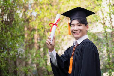 Gradende, mutlu bir Asyalı genç adam mezuniyet elbisesi giyiyor ve diploması var..