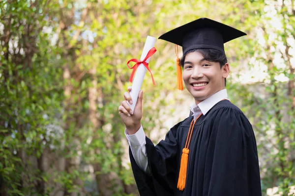 Gradende, mutlu bir Asyalı genç adam mezuniyet elbisesi giyiyor ve diploması var..