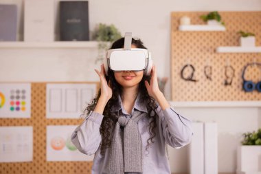 Modern çalışma stüdyosunda sanal gerçeklik gözlüğü takan Asyalı bir kadın. VR kulaklık kullanarak akıllı telefon.