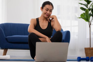 Asyalı kadın evde dinleniyor. Sabah yogaya başlayıp bilgisayarı açıp sınıfa katılıyorsun..