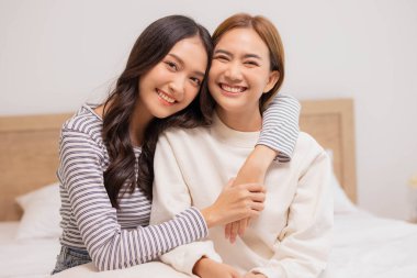 Mutlu LGBT lezbiyen çift yatakta sevgi ve romantizmle sarılıyor ve birlikte bakıyorlar..