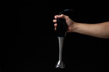 Siyah arka planda bir adamın elinde elektrikli blender. Yemek pişirmek için ev aletleri. Metin veya logo için bir yer var.
