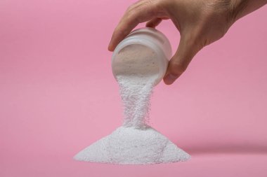 Pembe arka planda yıkama tozu. Çamaşır yıkamak için deterjan. Kutudan çamaşır tozu dökülüyor.