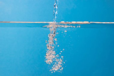 Su mavi bir zemin üzerinde suyun yüzeyine dökülür. Temiz içme suyu