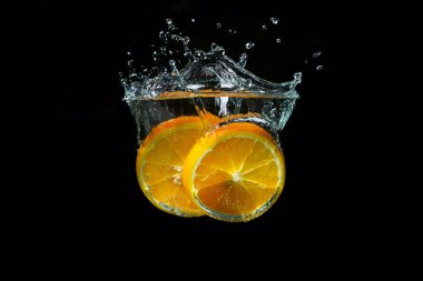 Portakal dilimleri siyah arka planda suya dökülüyor. Taze ve sulu portakal